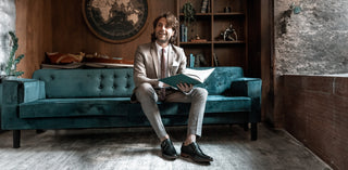Man sitting on teal couch reading a book wearing black monk strap dress shoes