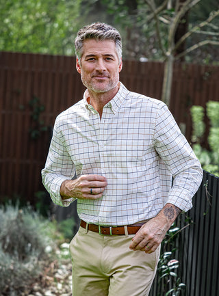 Male wearing casual check shirt and beige chinos standing next to wooden fence